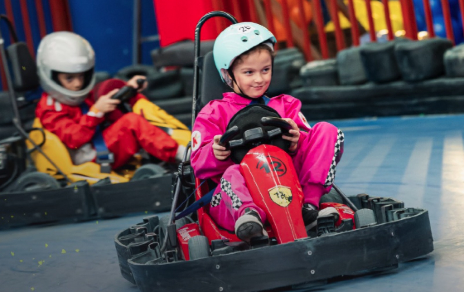 Menina sorrindo enquanto pilota um kart elétrico na pista indoor do eKarts