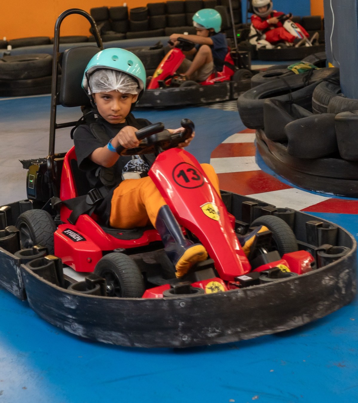 Menino concentrado ao volante do kart elétrico, com expressão de piloto de verdade na pista da eKarts