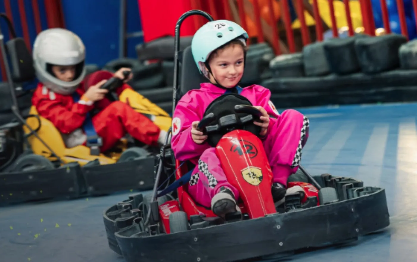 Menina de capacete rosa pilotando um kart elétrico na pista