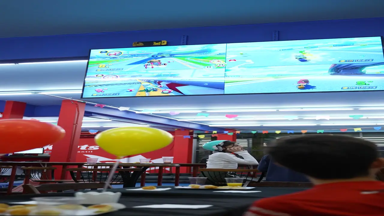 Telão com Mario Kart 8 na tela dividida, com crianças assistindo