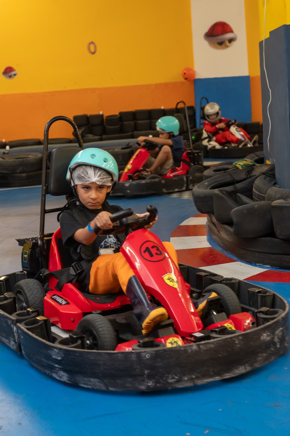 Menino concentrado ao volante do kart elétrico, com expressão focada de piloto profissional